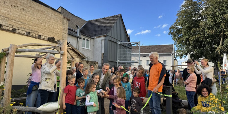 Der Bürgermeister steht in einer Gruppe mit Kindern. Gemeinsam schneiden sie ein gelbes Band durch zur offiziellen und feierlichen Eröffnung des PikoParks