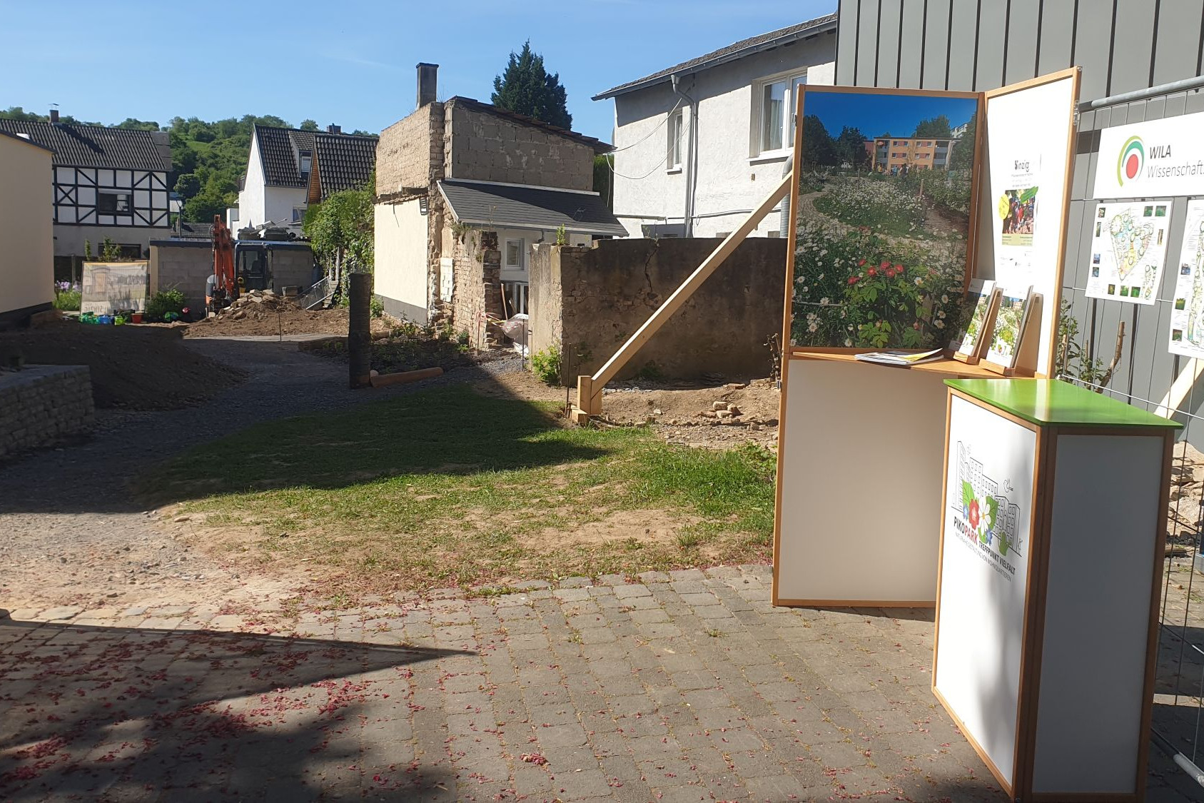 Blick auf eine Baulücke. Im Vordergrund ist ein kleiner weißer Infostand vom WILA Bonn zu sehen, der über den entstehenden PikoPark informier.