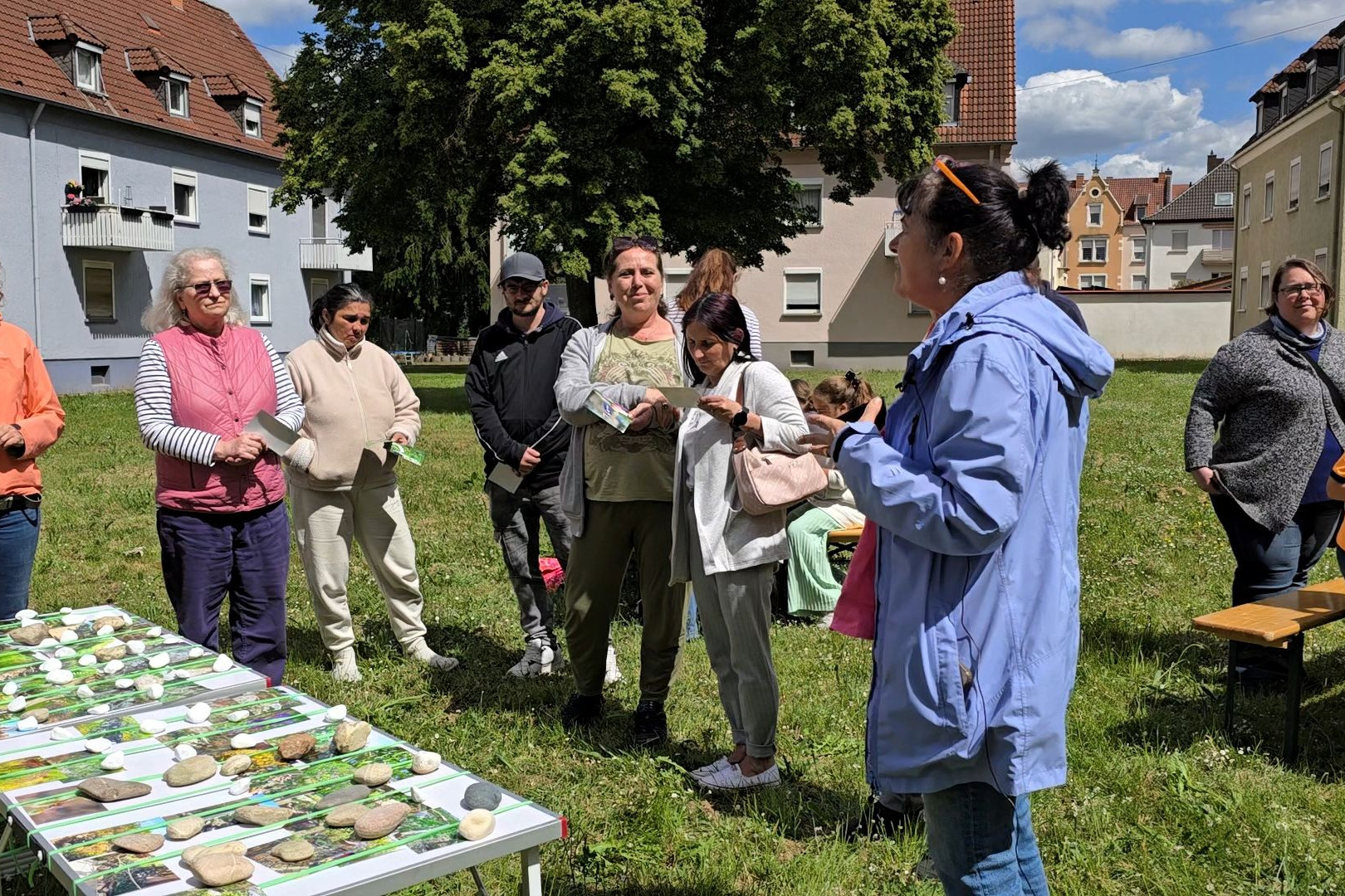 Erwachsene und Kinder stehen auf der Rasenfläche des zukünftigen PikoParks. Im Vordergrund ein Tisch mit sehr vielen Fotos mit naturnahen Gestaltungselementen
