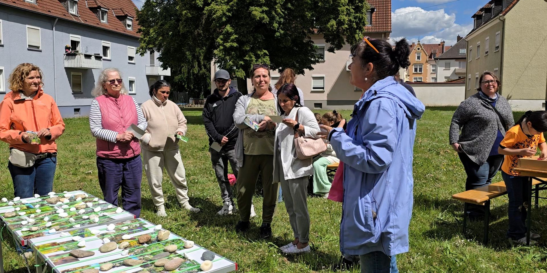 Erwachsene und Kinder stehen auf der Rasenfläche des zukünftigen PikoParks. Im Vordergrund ein Tisch mit sehr vielen Fotos mit naturnahen Gestaltungselementen