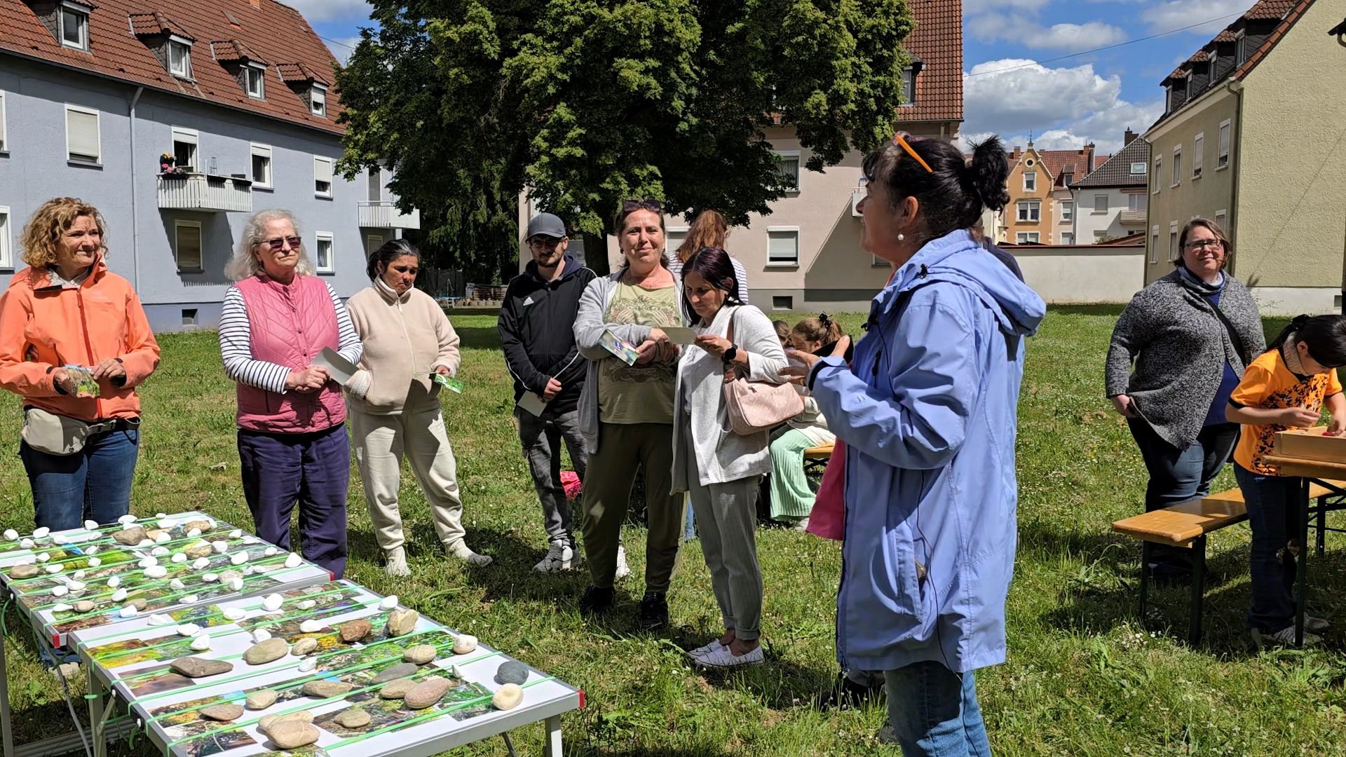 Erwachsene und Kinder stehen auf der Rasenfläche des zukünftigen PikoParks. Im Vordergrund ein Tisch mit sehr vielen Fotos mit naturnahen Gestaltungselementen