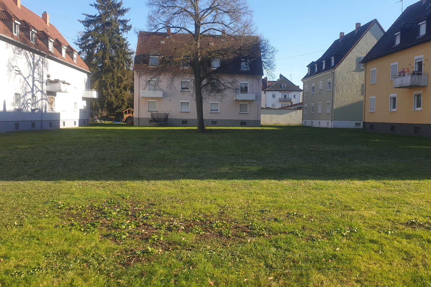 Blick auf eine Rasenfläche die rechts und Links und am Kopfende von dreigeschossigen Wohnriegeln eingerahmt ist